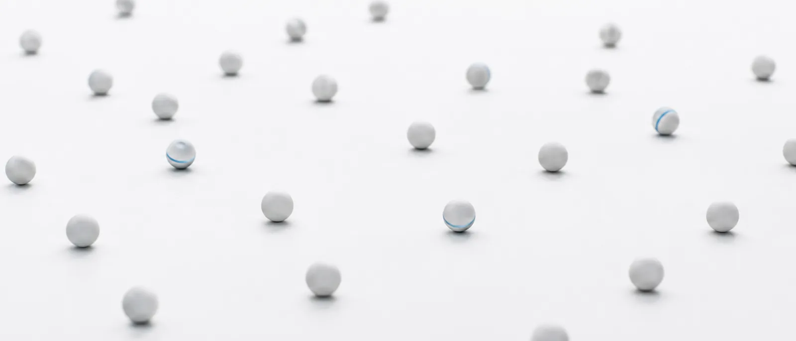 A field of identical white spheres with two blue marbles standing out among them.